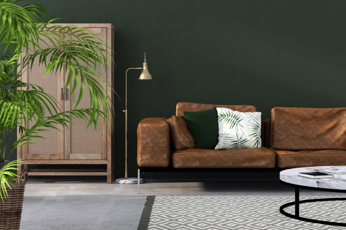 A small brown leather sofa with green throw pillows, plants and majesty palms on a wicker basket