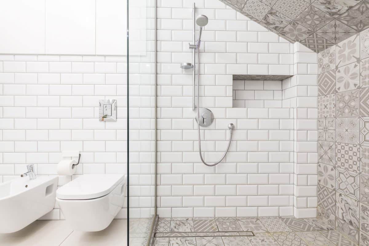A white brick tile wall with a glass walled shower area