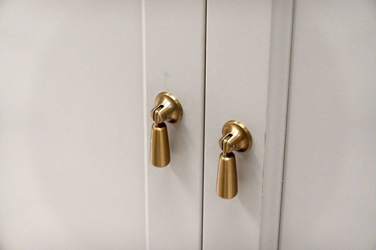 A wooden cupboard white kitchen door, brass metal handle details of furniture.
