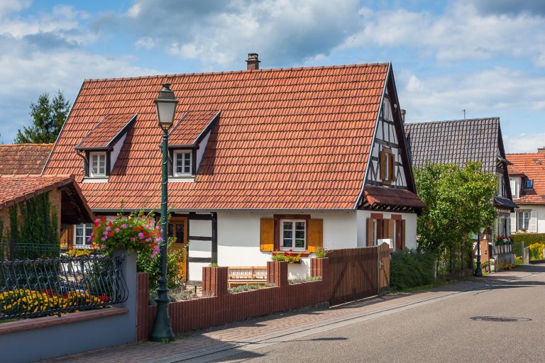 An English house with clay tile roofing, white windows trims and brown window shutters, What Color House Goes With A Brown Roof?