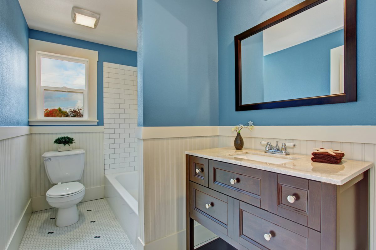 Bathroom interior with blue wall and white plank panel trim. Bath tub with tile wall trim.