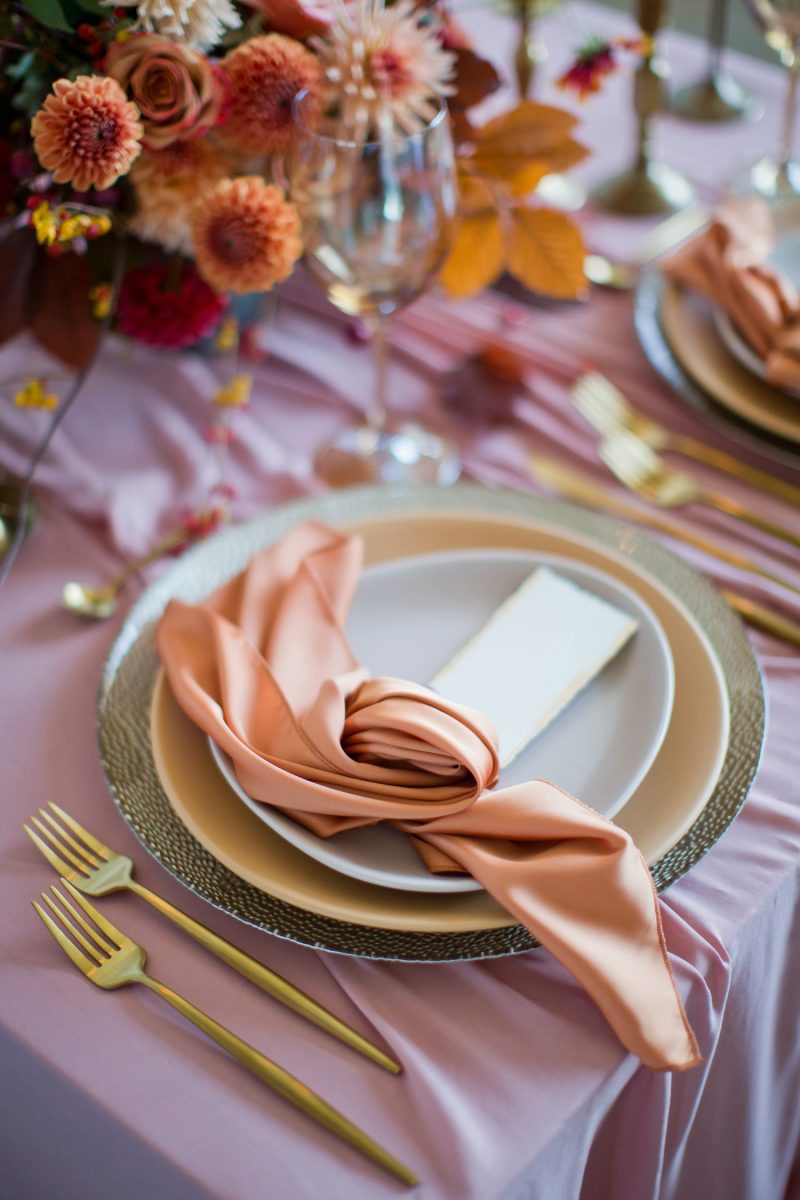 Beautiful table setting with autumn flowers, orange and pink napkins and burning candles. Autumn wedding concept

