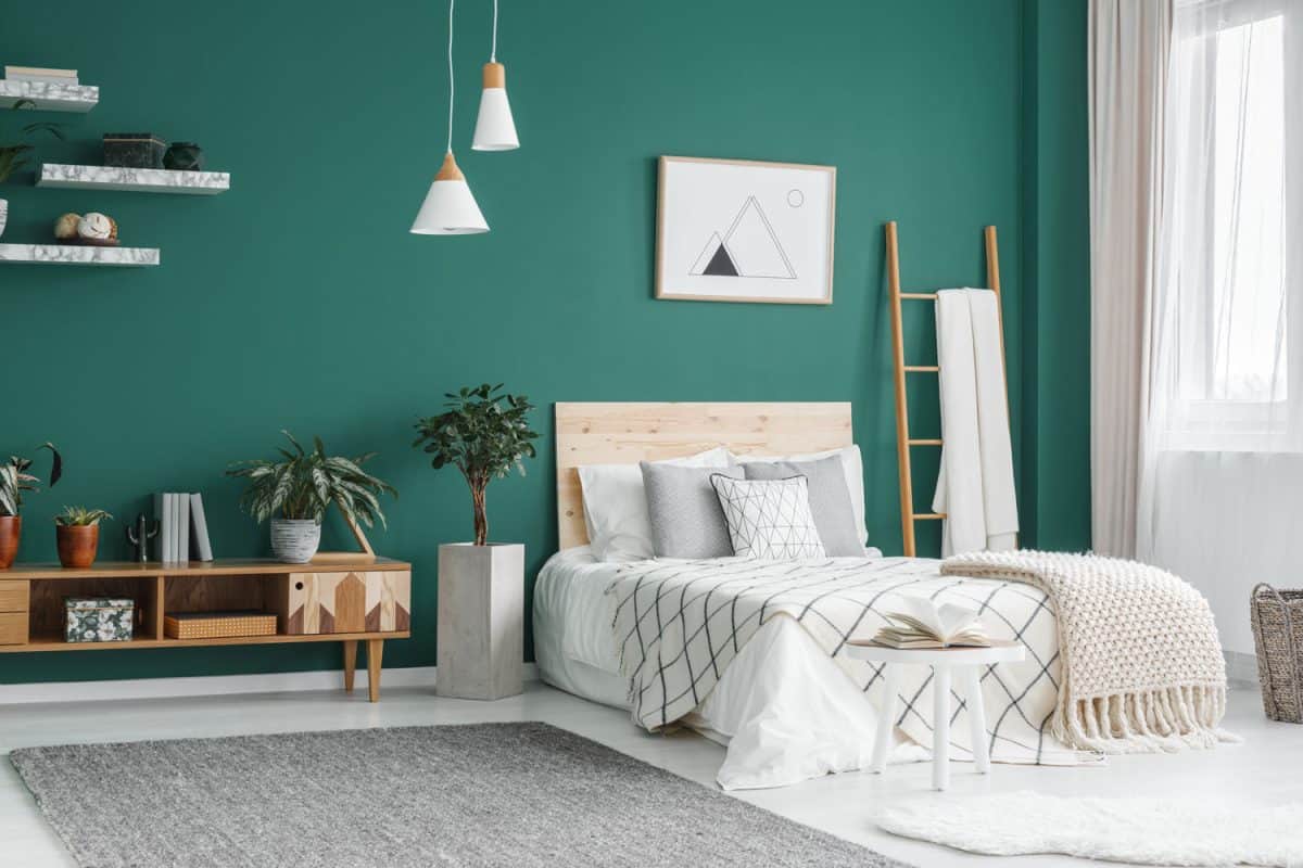 Bedroom with green wall matched with white beddings and wooden cabinets and dangling lamps
