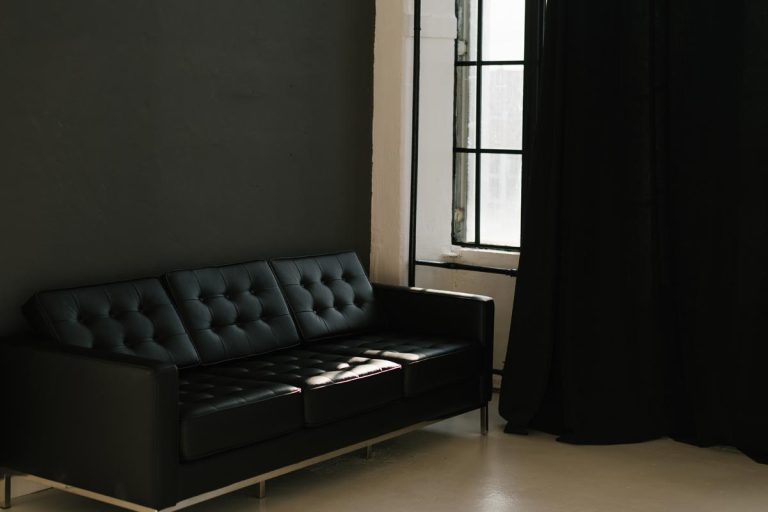 A brutal black sofa in a room with dark gray walls and black curtains on the window, What Color Curtains Go With Gray Walls And Black Furniture?
