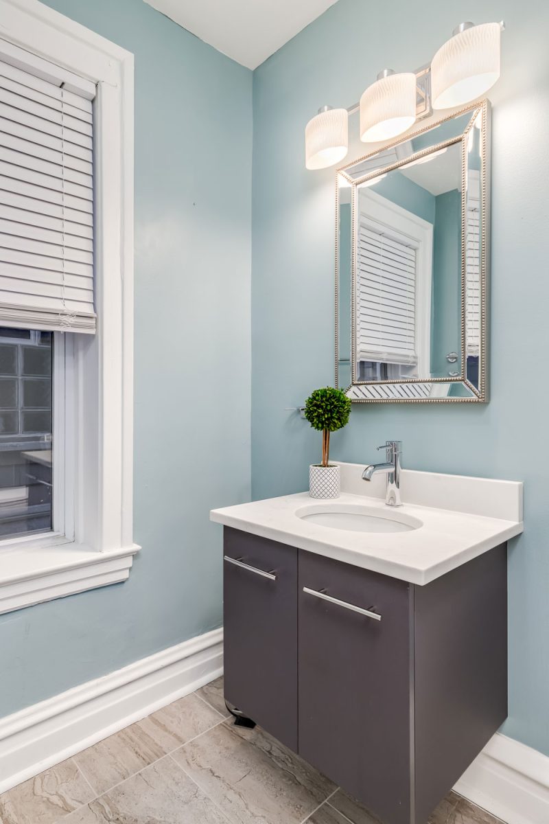 Classic modern bathroom with an aluminum cabinet and a blue painted wall with white trims on the window and baseboard