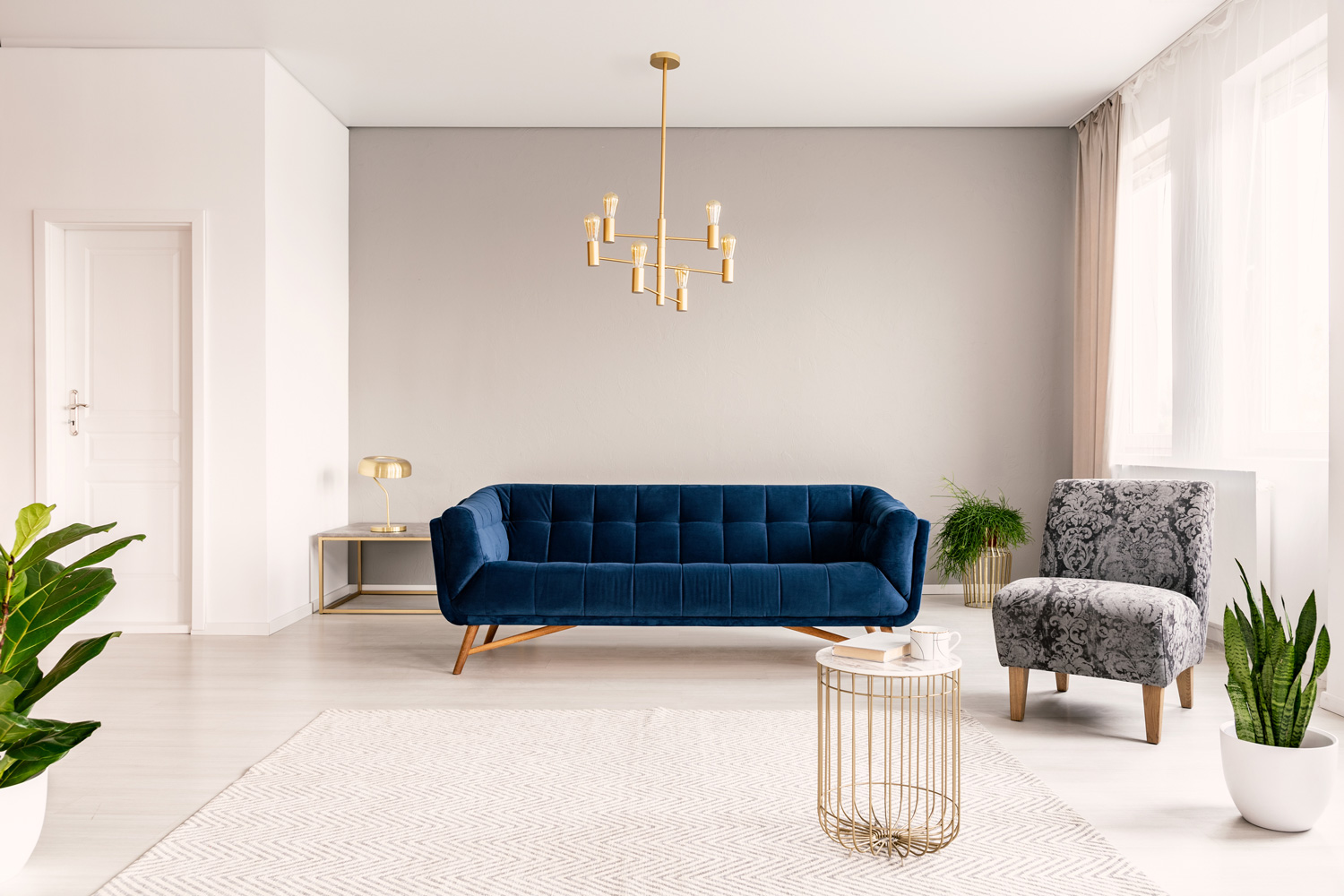 Copy space living room interior with a dark blue couch, a gray armchair and gold accents