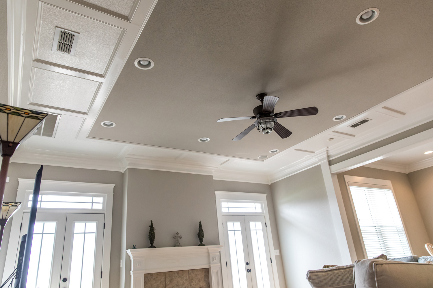 Detailed trim white wood tray ceiling with a ceiling fan in a beige greige gray new construction house