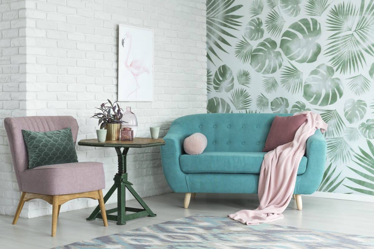 Green table with plant between pink chair and blue sofa in floral living room with wallpaper and poster

