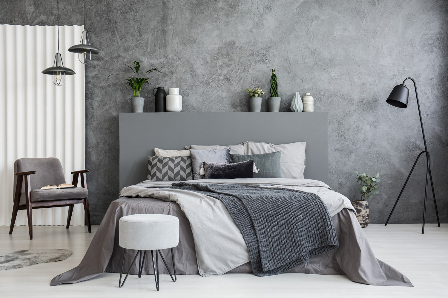Grey stool in front of bed with blankets and cushions in dark hotel bedroom interior.