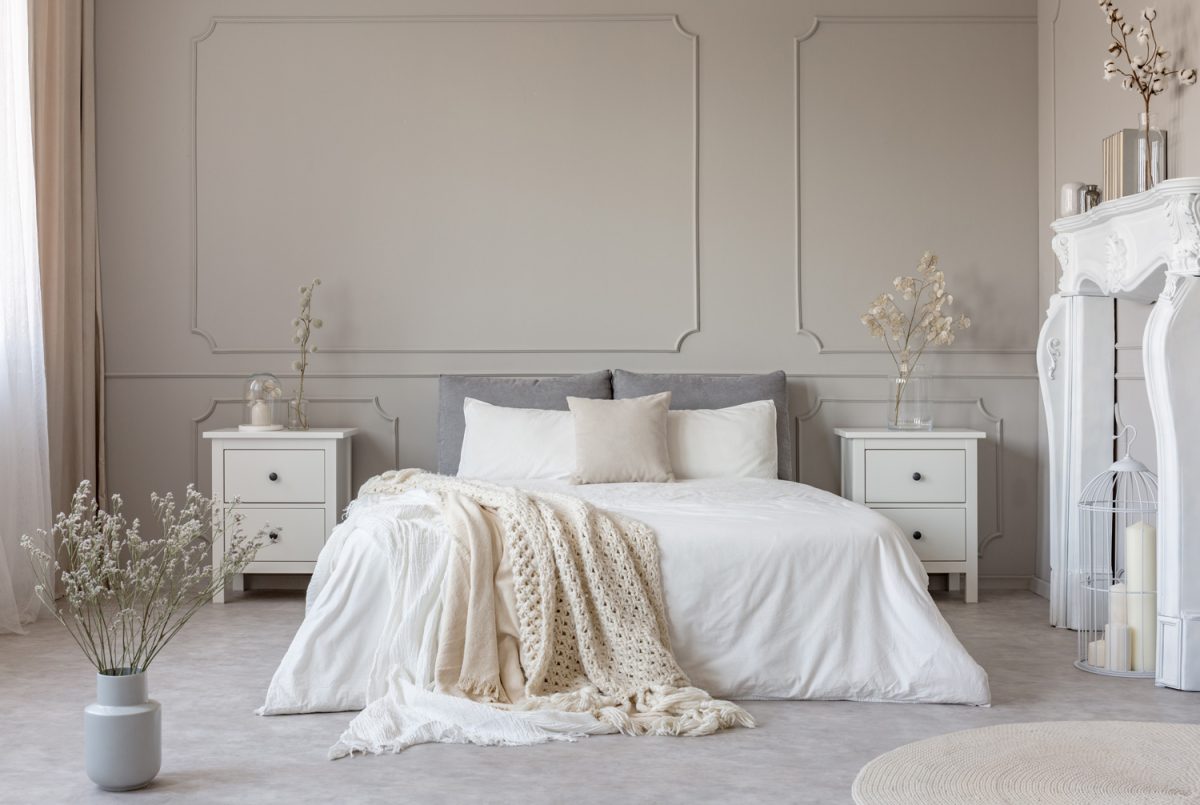 King size bed with white sheets and blanket between two wooden bedside tables flowers in vases
