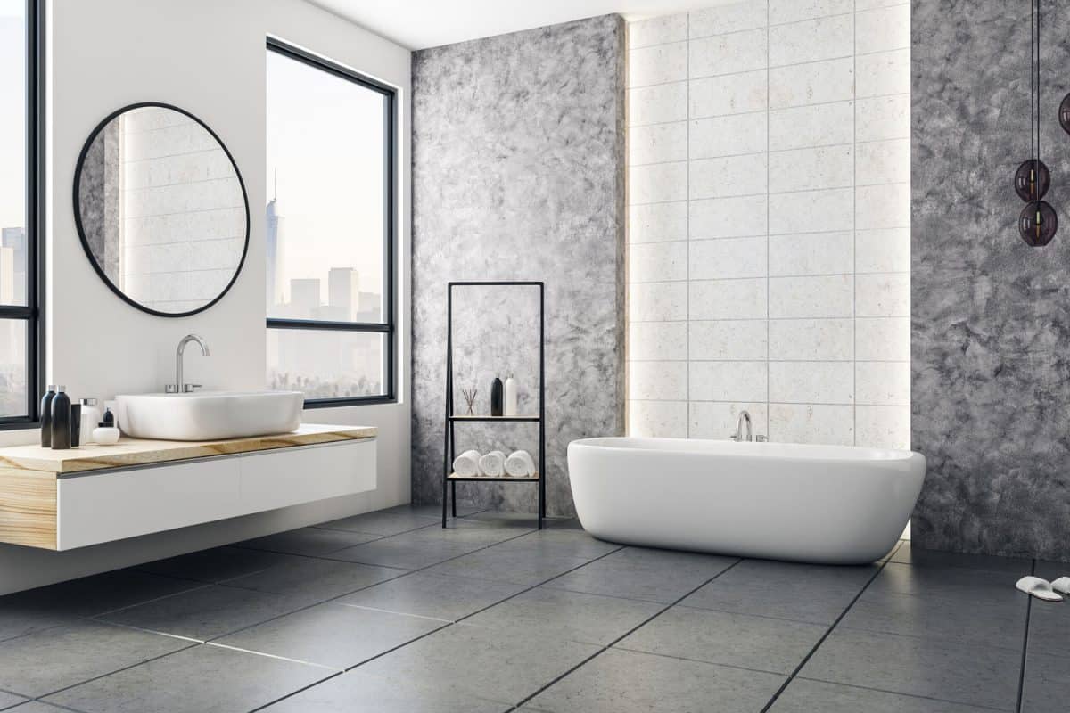 Luxurious modern bathroom with marble walls, gray tile flooring and a vanity with a round mirror and wooden vanity