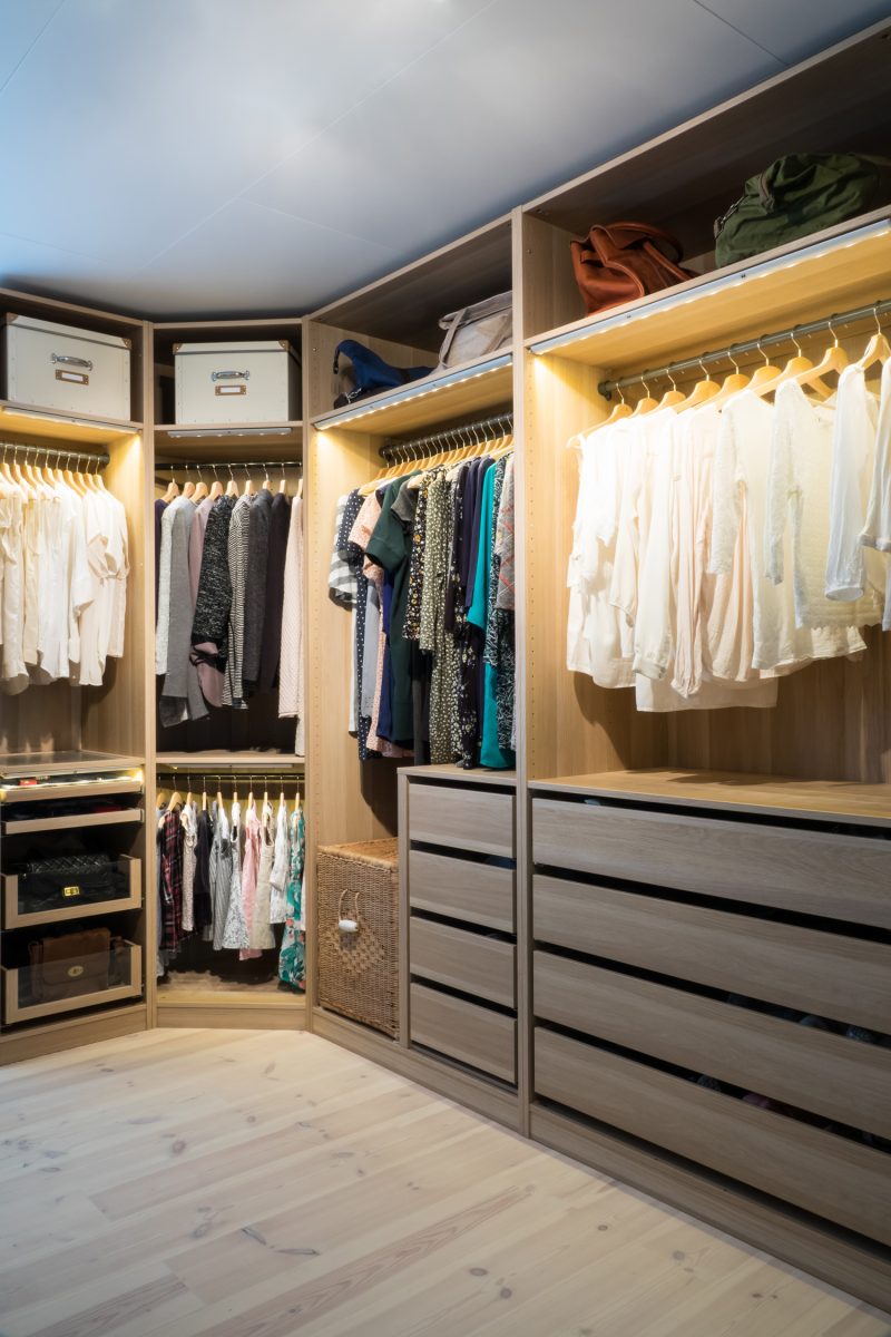 Luxury walk in closet / dressing room with lighting and jewel display. Dresses, handbags, blouses and sweaters on hangers in the wardrobe.