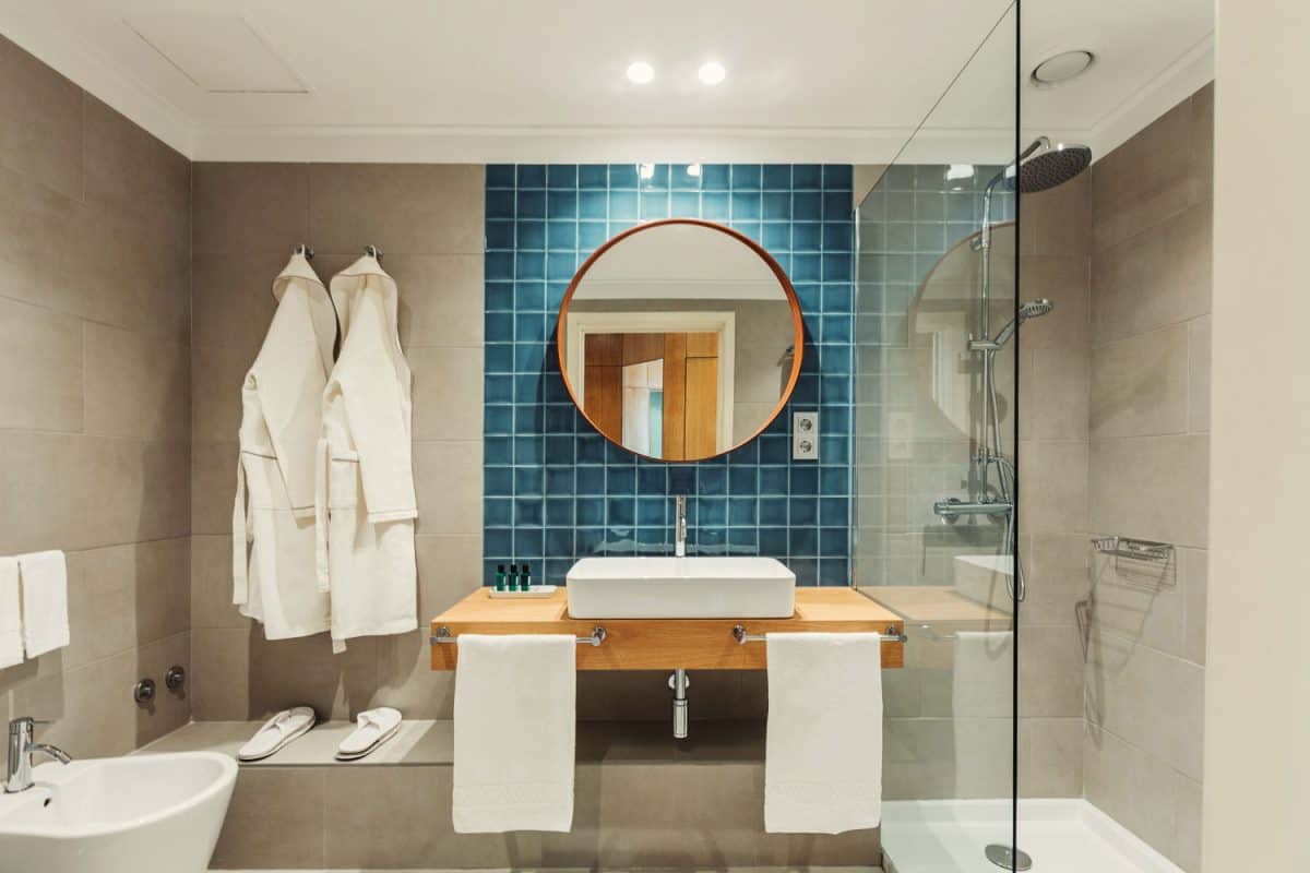 Modern contemporary bathroom with polished cement walls, a blue tile backsplash with wooden circular mirror