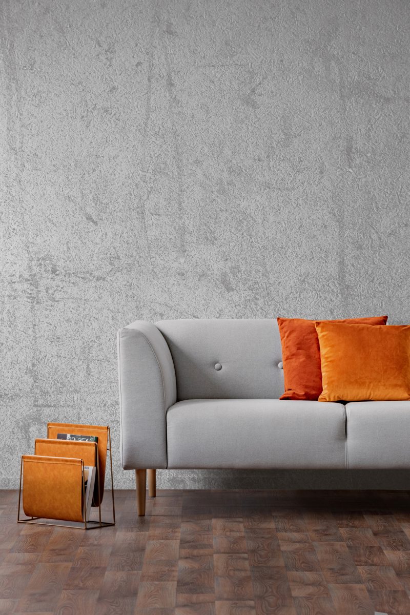 Orange pillows on grey settee in living room interior with concrete wall and wooden floor. Real photo

