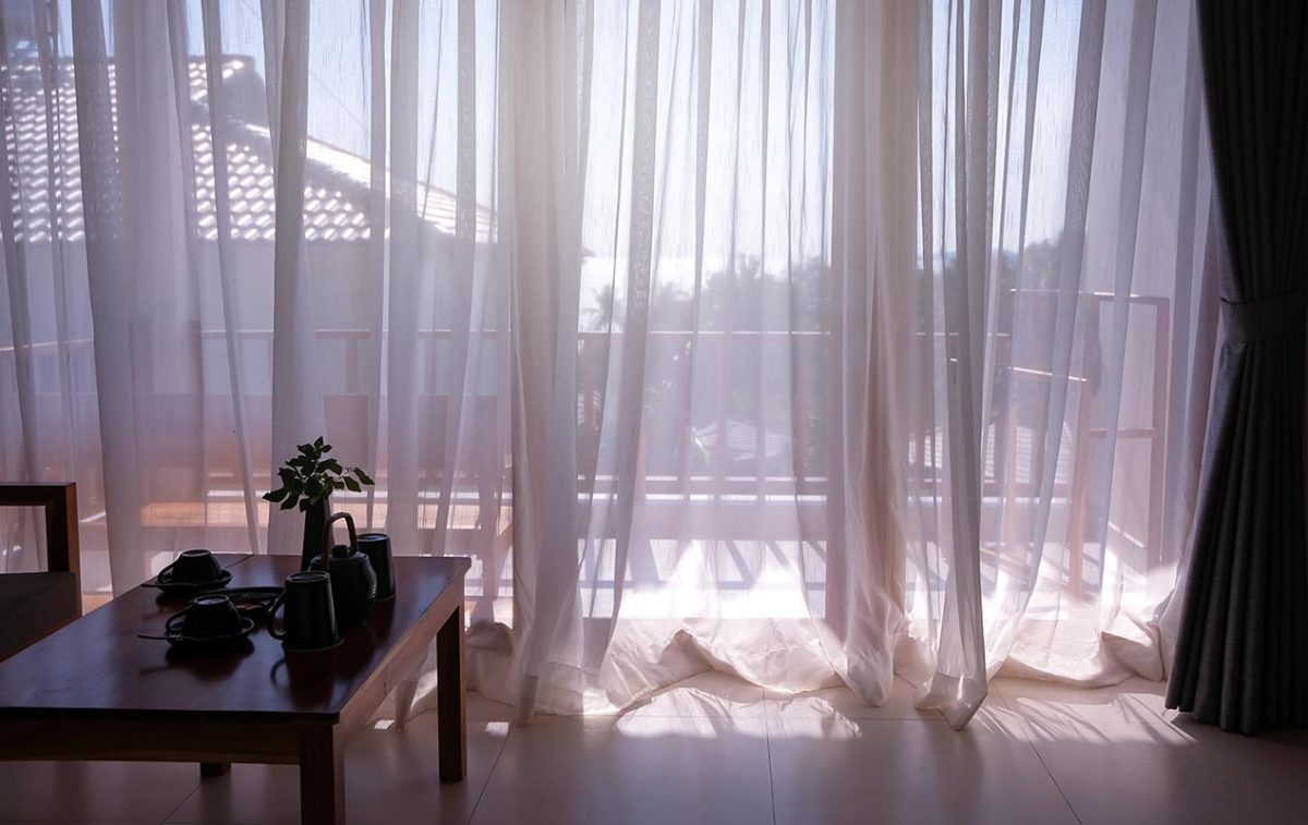 Partial view of sea seen through white translucent curtains at balcony window