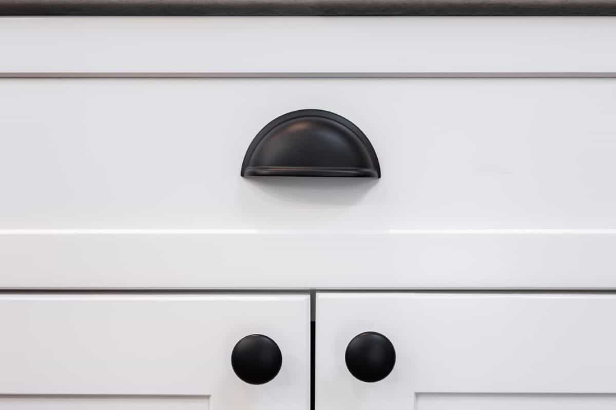 Photograph of a matte black drawer cup pull handle on a white cabinet.
