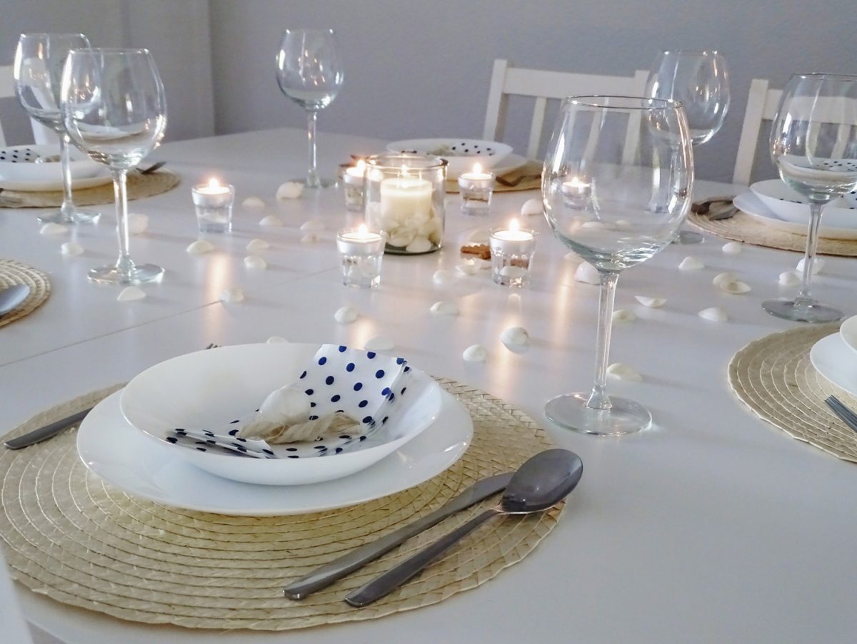 Table setting with seashells scattered throughout the table and with white napkins with dark blue polka dots. Everything decorated in beach style.

