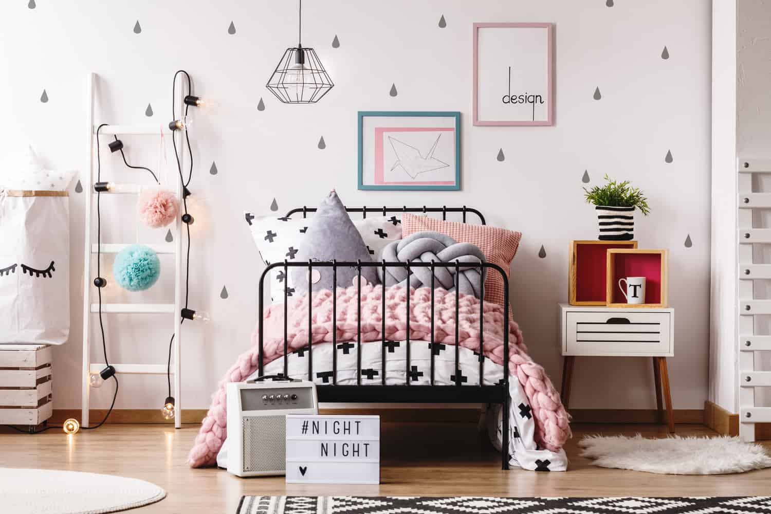 White ladder with pompons next to bed with shaped pillow in pastel child's bedroom with rugs