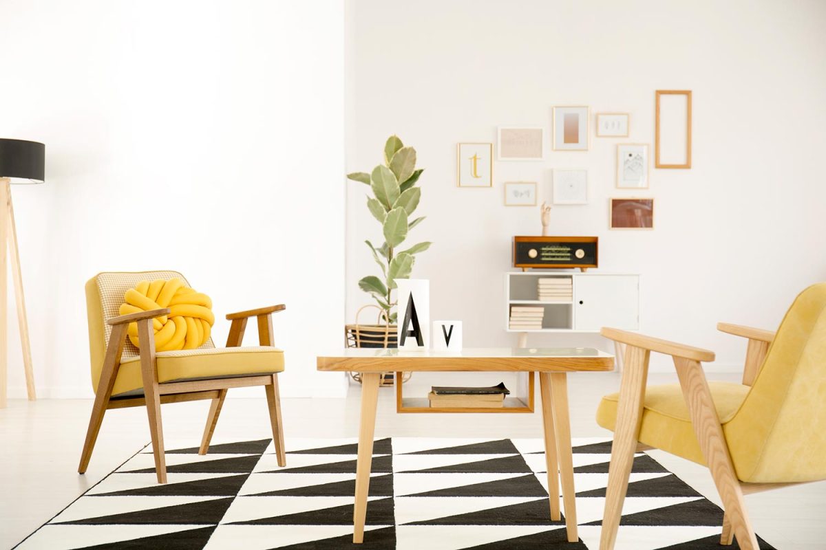 Wooden table and yellow armchairs on black and white carpet in vintage living room interior with ficus
