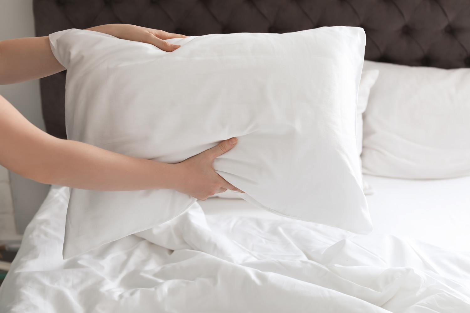 Young woman holding white pillow over bed, closeup